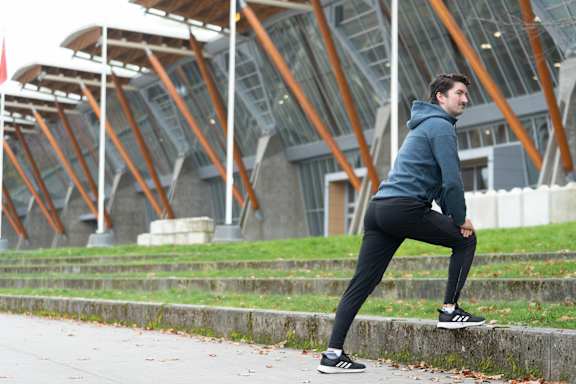 A man in a blue hoodie and black pants is stretching his leg.