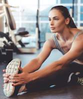 A woman is stretching her legs in a gym.