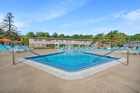 A large swimming pool with lounge chairs and a building in the background.