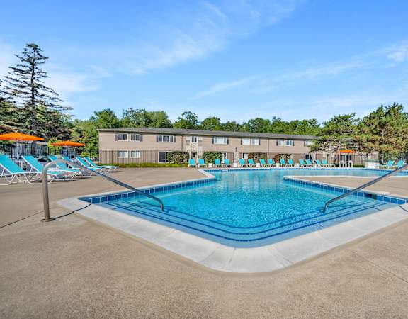 A large swimming pool in front of a building with lounge chairs around it.