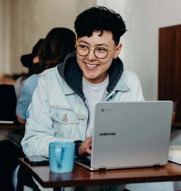 a young man sitting at a table working on a laptop computer