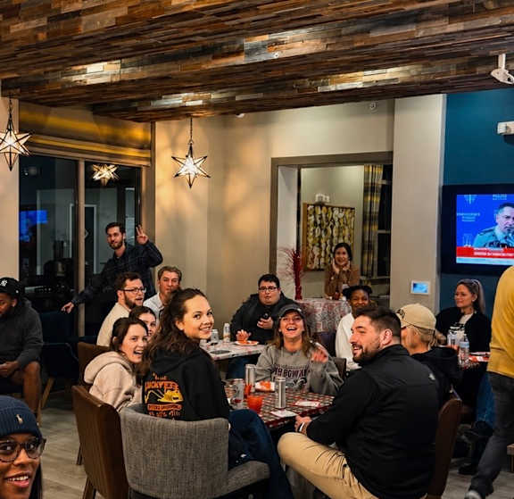 A group of people are sitting around a table in a room with wooden beams on the ceiling.