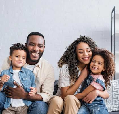 A family of four is sitting on a couch together.