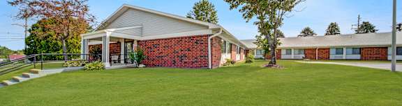 A building with a red brick wall and a white roof is surrounded by a green lawn. at Edinlake Apartments, Edinboro