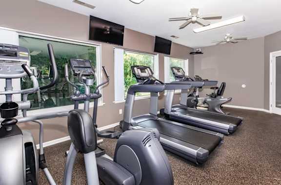 A spacious gym with treadmills, elliptical machines, and a television.