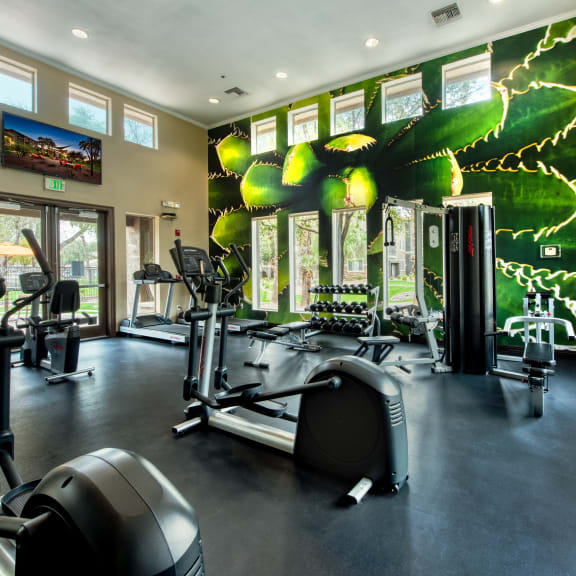 a gym with cardio equipment and a large wall mural of gym equipment
