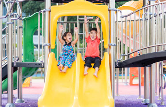 Two children playing on a yellow slide at a playground.