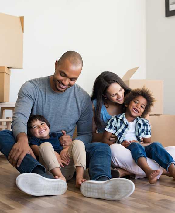 A family of four sitting on the floor surrounded by moving boxes.