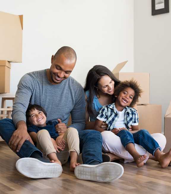 A family of four sitting on the floor surrounded by moving boxes.