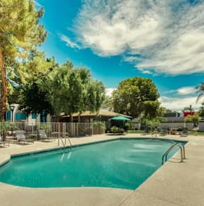 A large outdoor swimming pool surrounded by trees and a blue building. at Sycamore Square  Apartments, Arizona, 85202