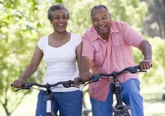 An older couple is riding bikes together in a park.