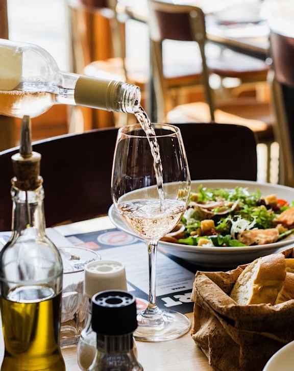 White wine being poured into a glass with a salad and bread on the table.