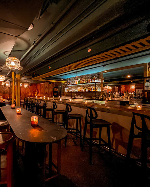 A bar with a long table and chairs with candles on the table.