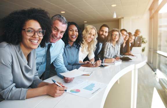 A group of people are gathered around a table, looking at a chart and discussing it.