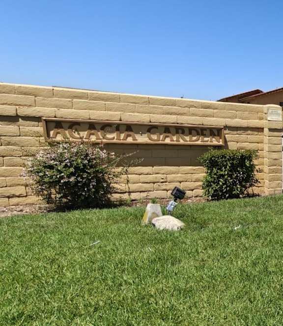 A dog is sitting in the grass in front of a stone wall with a sign that reads "Rosalita's Garden".