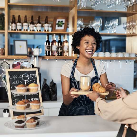 A woman in an apron is serving food to a customer at a counter.