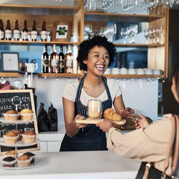 A woman in an apron is serving food to a customer at a counter.
