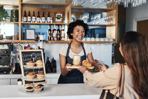 A woman in an apron is serving food to a customer at a counter.