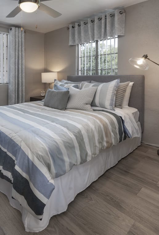 Bedroom with two large windows, fan, wood-style floor, and model furnishings at Terraces at Clearwater Beach, Florida