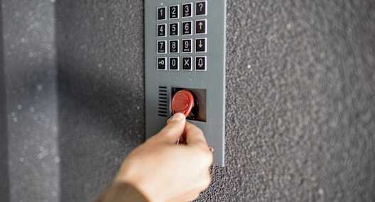 A person is pressing a red button on a grey wall.