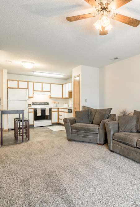 a kitchen with white appliances, vinyl flooring, and a living room with couch and chiar