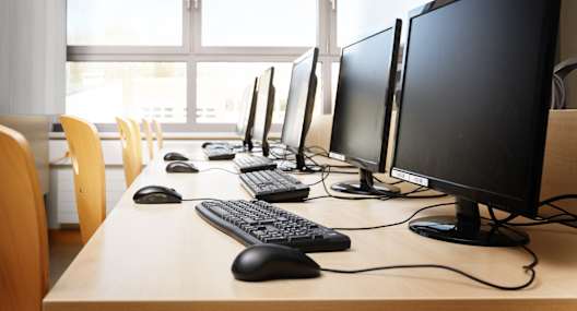 A row of computer monitors are lined up on a desk.