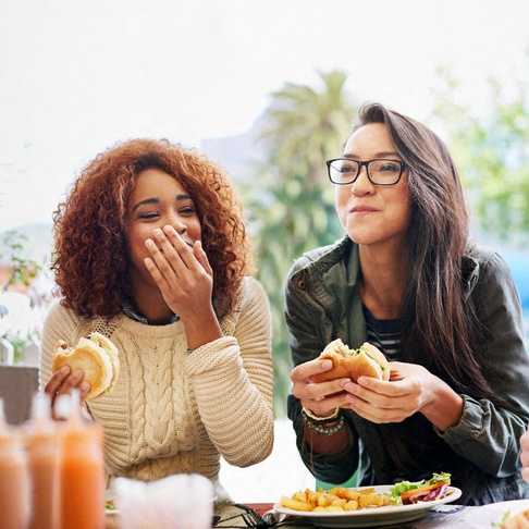 Three people eating sandwiches at an outdoor table.