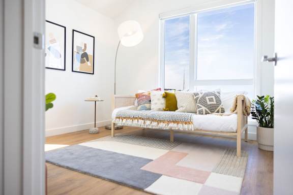 A white couch with pillows and a blanket is in the center of a room with a large window.