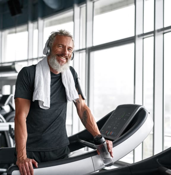a man with a towel around his neck running on a treadmill in a gym at The Woods, Kanata, Ontario
