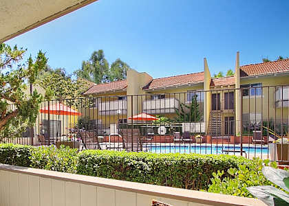 A patio with a table and chairs overlooks a pool and a building.