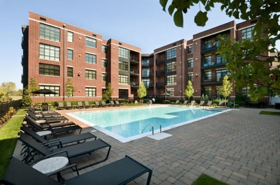 a swimming pool with chaise lounge chairs and trees in front of a brick building