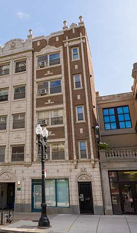 A tall building with many windows is in the middle of a street.