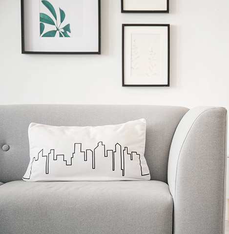 A grey couch with a white pillow that has a city skyline design on it.