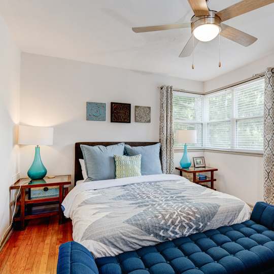 A bedroom with a bed, a ceiling fan, and a blue chair.