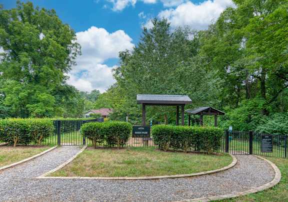 A small pavilion is surrounded by a hedge and a gravel path.
