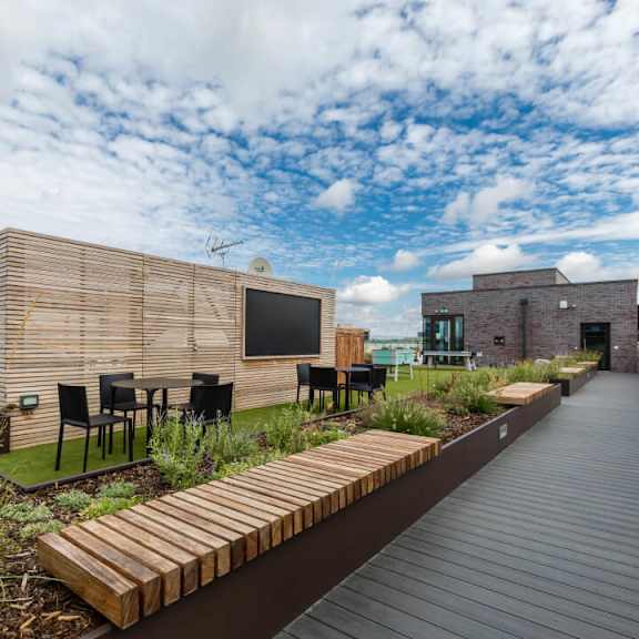 A modern outdoor seating area with a wooden deck and black chairs at Beton Apartments, Wembley, HA9 0SL