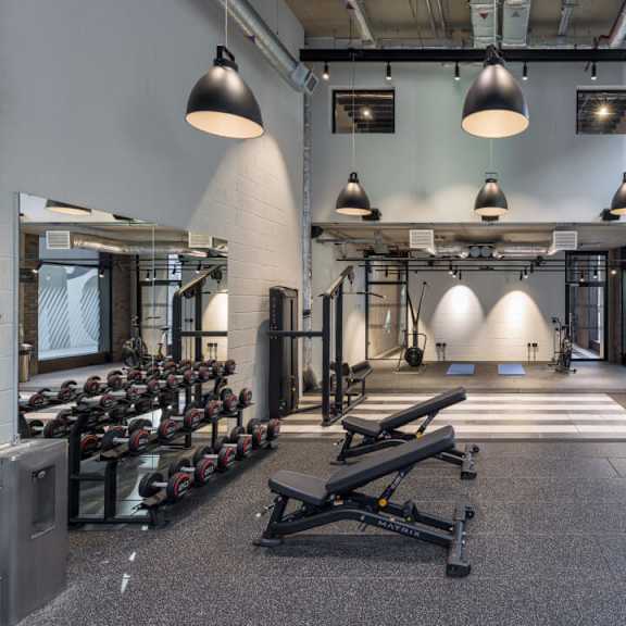 A gym with a row of dumbbells on the left and a bench press on the right at Beton Apartments, Wembley, HA9 0SL