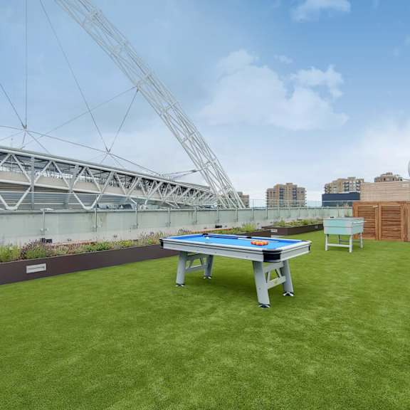 A pool table is set up on a grassy area with a large crane in the background at Beton Apartments, Wembley, HA9 0SL