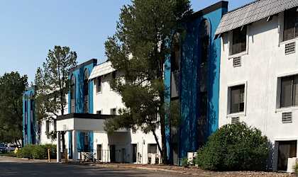 A white building with blue accents and a tree in front.
