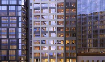 A modern building with a curved glass facade stands next to a building with a grid-like facade.