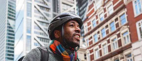 A man wearing a grey sweater and a multicolored scarf is riding a bicycle on a city street.