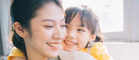 A woman in a beige sweater is holding a child in a yellow top.