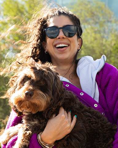 A woman in a purple sweater is holding a brown dog.