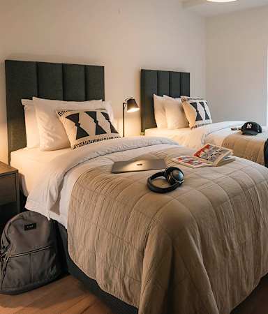 A bed with a white comforter and a black headboard with a white pillow and a black cap on the bed.