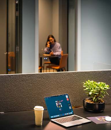 A laptop with a blue screen is on a desk with a coffee cup and a plant.