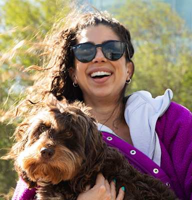 A woman in a purple sweater is holding a brown dog.