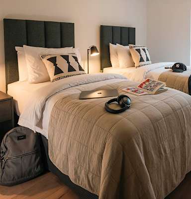 A bed with a white comforter and a black headboard with a white pillow and a black cap on the bed.