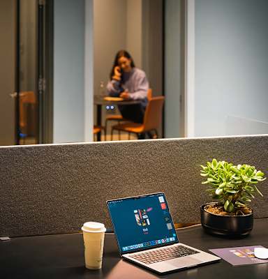 A laptop with a blue screen is on a desk with a coffee cup and a plant.