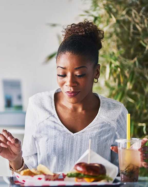 A woman is eating a burger and drinking a beverage.