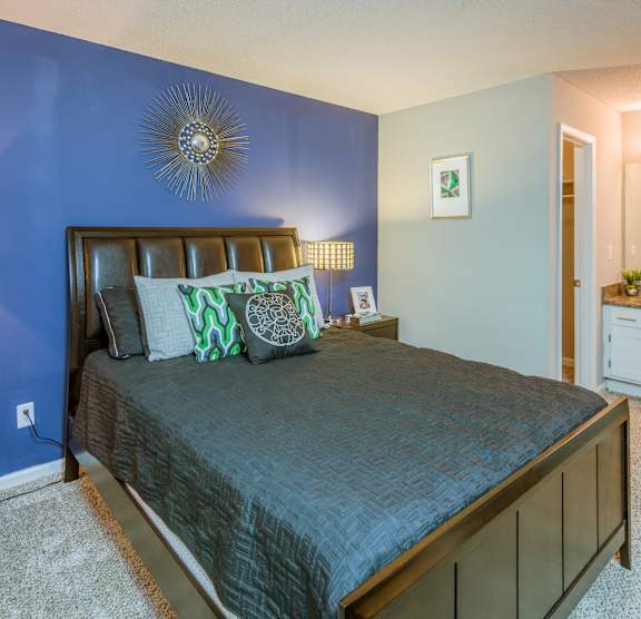 A bedroom with a bed, a lamp, and a mirror. at The Colony at South Park, Aiken